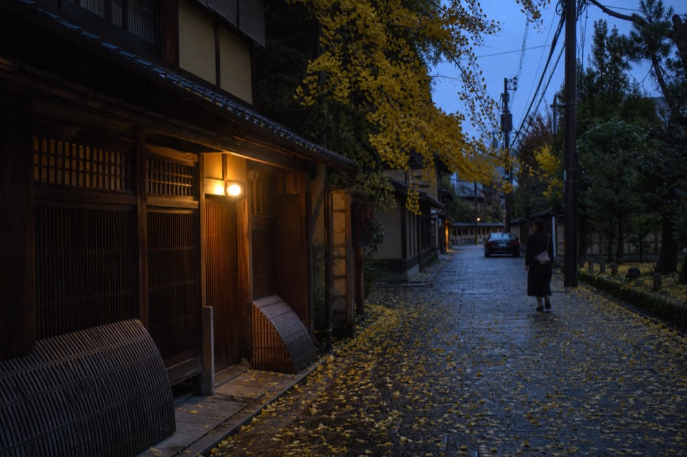 A traditional wooden teahouse facade with closed lattice windows and a stone lane in Gion at dusk
