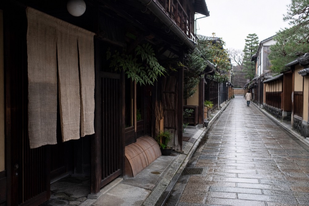 Quiet stone-paved lane in Kyoto with wooden houses and hanging noren curtains