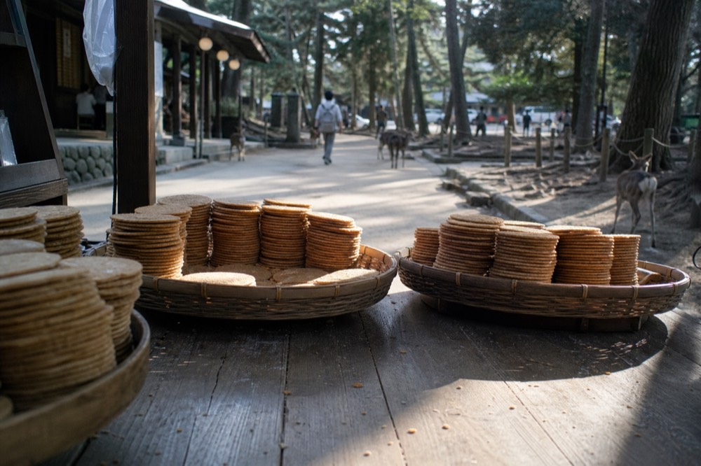 Stacked rice crackers for sale at a wooden stall beside a park path