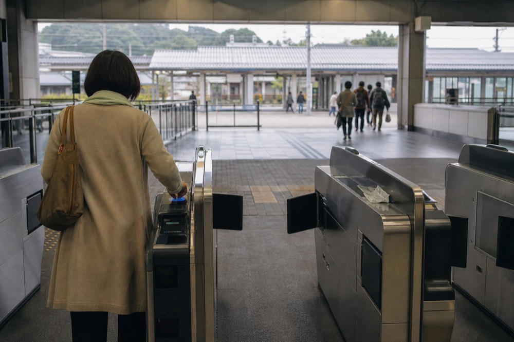 A rail station ticket gate with a passenger tapping a contactless IC card