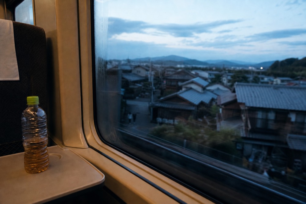 A train interior view looking toward Kyoto rooftops through the window